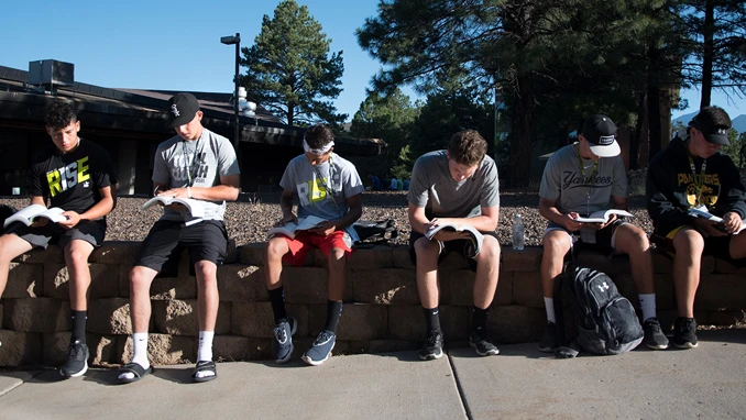 Group of students sitting on a stone wall reading Bibles.